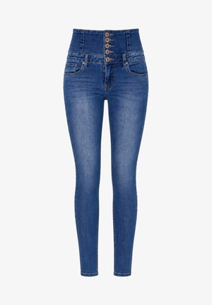 Kvinde iført højtaljede blå denimjeans med fem synlige kobberknapper og forlommer, vist fra taljen til de øverste lår.