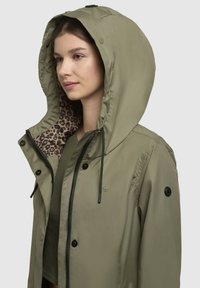 Olijfgroene gewatteerde jas met een luipaardprint voering, zwarte hardware en trekkoorden. Voorzien van een ritssluiting met drukknoopsluiting.