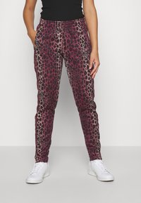 Kalhoty s leopardím vzorem v barvách vínová a černá, s elastickým pasem, bočními kapsami a zúženými nohavicemi. Kombinované s bílými teniskami.
