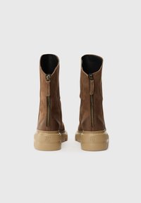 Brune skinn ankelsko med glidelås på siden, lav beige gummisåle og rund tå. Glatt tekstur med subtile sømdetaljer.