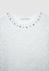 Maglione bianco morbido con collo rotondo, decorato con gemme trasparenti lungo il collo. Texture morbida, vestibilità rilassata e senza motivi visibili.