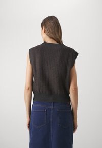 Mørkegrå ærmeløs strikket top med vertikal ribb i maroon nuancer, parret med en blå denimnederdel, set bagfra.