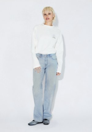 Wit shirt met lange mouwen en een kleine afbeelding, gecombineerd met lichtblauwe wijde spijkerbroeken en zwarte schoenen. Glad stof, comfortabele pasvorm en casual stijl.