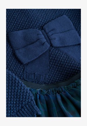 Top de punto navy con patrón texturizado, que presenta un gran detalle de lazo. El dobladillo es Volante con tejido azul oscuro en capas y cinturilla elástica.