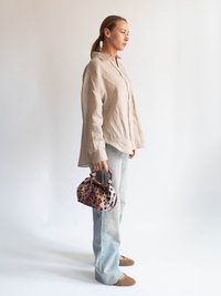 Camicia button-up in lino beige, jeans svasati blu chiaro e borsa a tracolla con stampa leopardata marrone, con parte superiore arricciata e manico circolare.