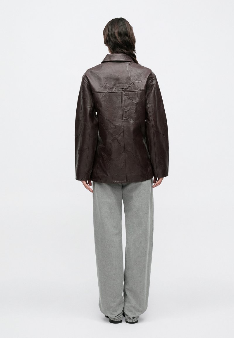 Veste en cuir marron à texture froissée, design à col et coupe droite. Assortie à un pantalon gris ample pour un look décontracté.