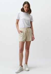Beige broek met trekkoord, voorzien van twee zijzakken, gemaakt van lichtgewicht stof. Gepaard met een simpel wit T-shirt en witte sneakers.