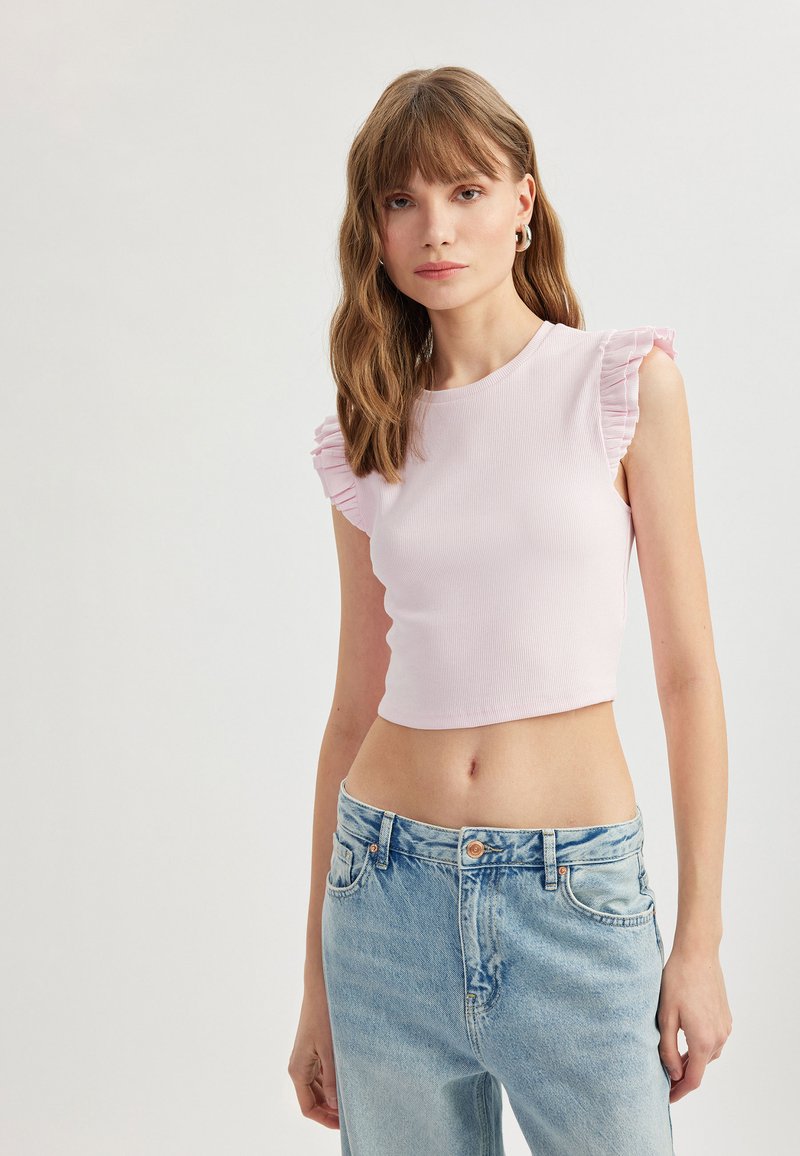 Lichtroze geribbelde crop top met ruche mouwen, gecombineerd met lichtblauwe high-waisted jeans. Soepele textuur, aansluitend ontwerp.