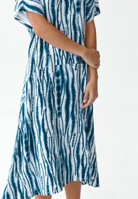 Väljande klänning i lätt tyg, med blå och vita vertikala ränder och ett tie-dye-mönster. Ärmarna är i armbågs-längd.