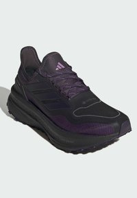 Chaussure de course violette avec un dessus texturé, dotée de trois bandes, de lacets et d'une semelle robuste. Fabriquée en matériaux synthétiques avec des accents étanches.