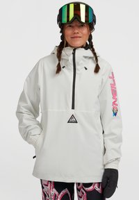 Witte pullover jack met zwarte rits, elastische manchetten en roze logo-accenten. G gedragen met een patroonbroek en skibril. Waterdicht materiaal.