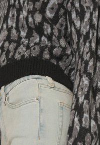 Stickad svart och grå mönstrad tröja med ribbad nederkant, i kombination med ljusblå denimjeans med synlig ficka och sömnadsdetaljer.