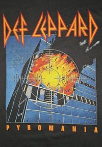Černé tričko s barevným motivem budovy s explozí, kříži zaměřovače a textem "DEF LEPPARD PYROMANIA" červenou a oranžovou barvou.