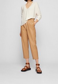 Pull crème clair à col en V associé à un pantalon paperbag couleur fauve. Des sandales marron à lanières avec une semelle épaisse noire complètent la tenue.