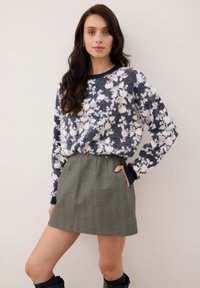 Trui met bloemenpatroon in marineblauw en wit, gecombineerd met een groene tweed rok. De trui heeft ribgebreide manchetten en een onderkant; de rok heeft zijzakken.