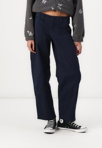 Calças largas azul marinho com fecho de botão, apresentando bolsos laterais e uma textura de algodão suave, combinadas com ténis pretos.