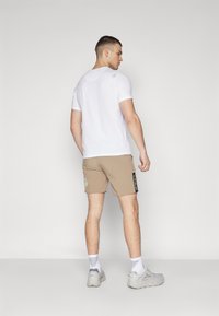 Vit tajt t-shirt och ljusbruna shorts med ett mönstrat detalj på sidan. Outfitten kompletteras av grå idrottsskor.