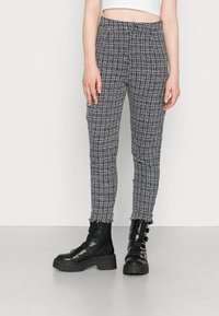 Calças xadrez em preto e branco com um tecido texturizado, apresentando bainhas desfiadas e um design ajustado, combinadas com botas de combate pretas e robustas.