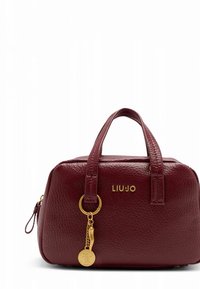 Borsa a mano in pelle bordeaux con finitura testurizzata, forma arrotondata, manici corti, ferrature dorate e un ciondolo con targhetta logo.