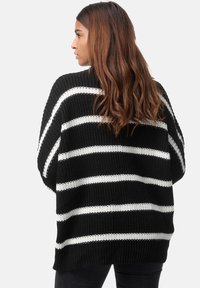 Pullover in maglia a righe bianche e nere con una vestibilità ampia, caratterizzato da un ampio scollo e spalle cadenti. Tessuto texture con orlo a costine.