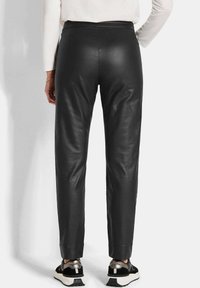 Pantalons en cuir noir au design ajusté, avec une texture lisse, des jambes fuselées et une taille élastique, associés à des baskets noires et argentées.
