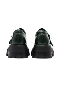 Paire de chaussures à plateforme en cuir vert foncé avec semelles crantées noires épaisses, vues de dos sur fond blanc.