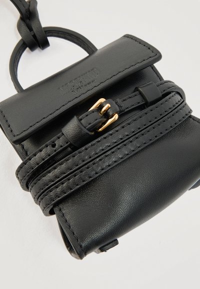 Μικρή τσάντα χειρός από μαύρο δέρμα με καπάκι, ραφές, ρυθμιζόμενο λουρί με χρυσή αγκράφα και εμφανούς τύπου σήμανση του ονόματος της μάρκας στο επάνω καπάκι.