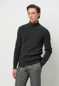 Dunkelgrauer, gerippter Rollkragenpullover aus strukturiertem Strickmaterial, kombiniert mit hellgrauen, maßgeschneiderten Hosen. Einfaches und modernes Design.