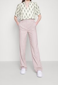 Blouse légère en crème avec un motif de feuilles, col froncé. Associée à un pantalon ample rose pâle et des baskets blanches.