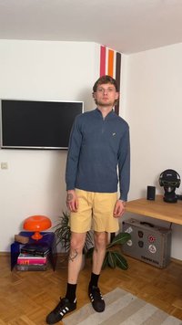 Jūras spēku zips garām piedurknēm, bēšas šortus, melni sporta apavi ar baltām svītrām. Minimālistisks dizains, brīvas formas piegriezums, attēlots iekštelpu vidē.