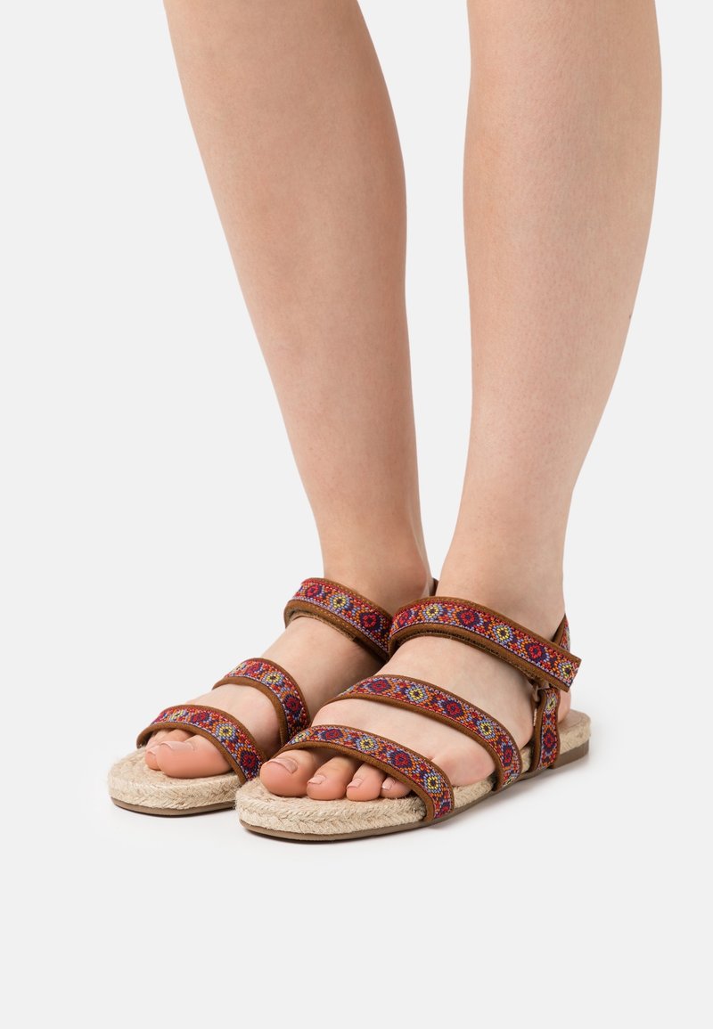 Sandali espadrille marroni con cinturini intrecciati multicolori, suola piatta, design con punta aperta, che mostrano motivi ricamati lungo i cinturini.