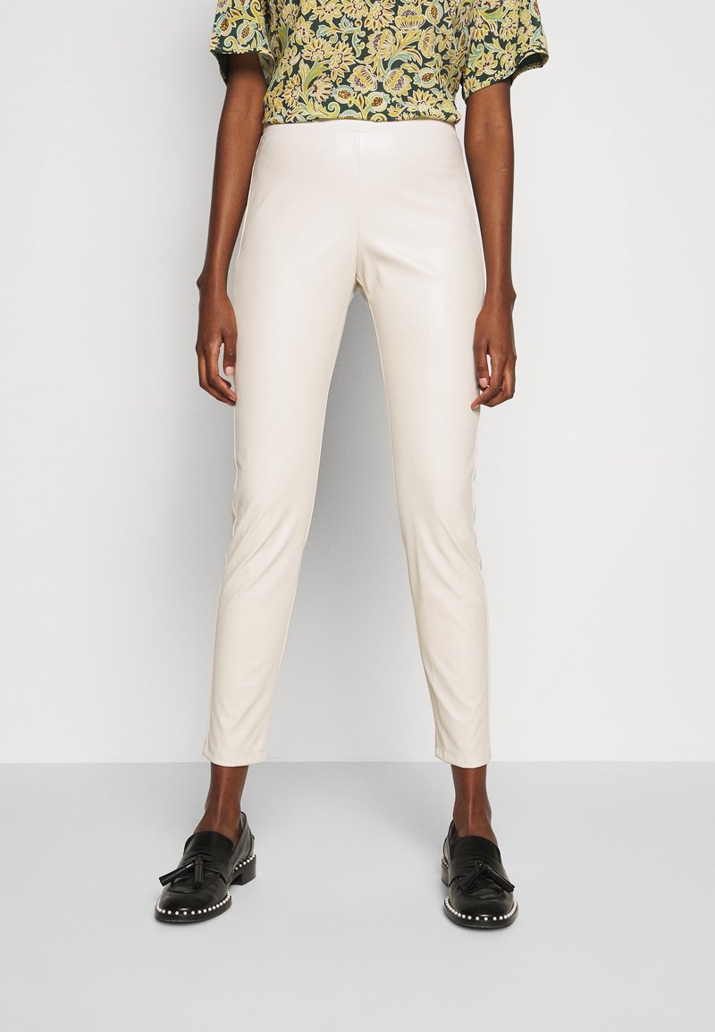Pantalon beige skinny en cuir synthétique à la texture lisse, avec une coupe slim et une taille haute, associé à un haut vert à motif.