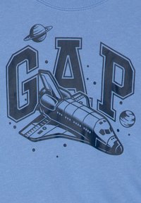 Světle modré tričko s grafikou vesmírné rakety a planet, s nápisem "GAP" v tučných černých písmena.