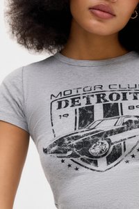 Žena nosi sivi majicu s vintage crnim grafičkim prikazom automobila i tekstom "Motor Club Detroit".