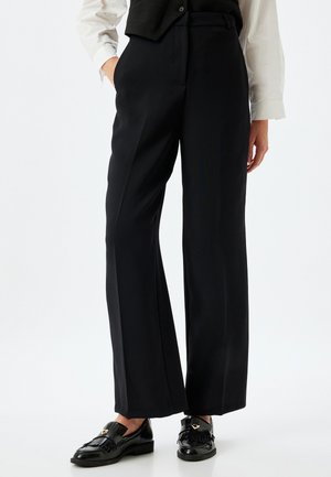 Pantaloni a gamba larga neri realizzati in tessuto morbido, con vita alta e tasche laterali. Abbinati a mocassini neri in vernice.