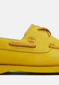 Gula lädersneakers för båt med en slät yta, som har bruna detaljer, rundad tå och synlig sömnad. Logotyp inpräntad på den laterala sidan.
