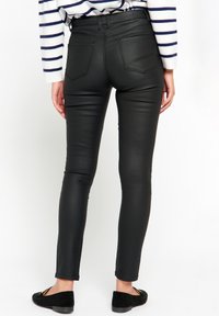 Čierne skinny nohavice z umelej kože s vysokým pásom, majúce zadné vrecká a hladkú textúru, v kombinácii s čiernymi šľapkami.