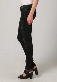 Jeans ajustados negros con paneles laterales texturizados y cintura alta. Combinados con sandalias negras de tacón con un detalle de hebilla.