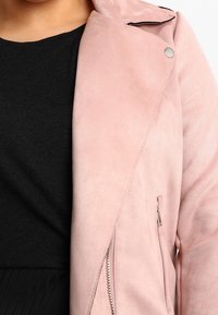 Jasnoróżowa zamszowa kurtka z ukośną kieszenią na suwak i czarnym przeszyciem dekoracyjnym. Posiada kołnierz z wycięciem i srebrne zatrzaski.