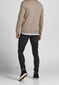 Jeans negros ajustados y un sudadera beige, de tejido suave, con cuello redondo y puños acanalados. Zapatillas negras de caña alta con detalles en blanco.