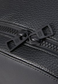 Black textured leather bag featuring a double zipper with square pull tabs and fine stitching along the edges for durability.