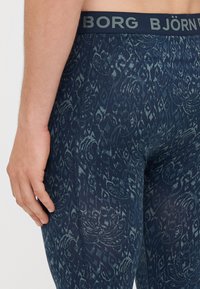 Marineblaue Leggings mit floralem Muster, ausgestattet mit einem dunkel gefärbten elastischen Bund, der mit "BJÖRN BORG" beschriftet ist. Sehr glatte Textur mit dehnbarem Material.