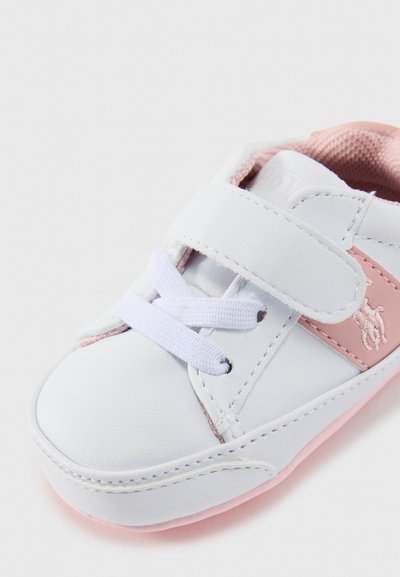 Baskets en cuir blanc avec une sangle Velcro, des accents roses et une semelle en caoutchouc rose doux. Présente des lacets et un détail de logo en relief sur le côté.
