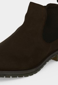 Bottine Chelsea en daim marron foncé avec panneau latéral élastique noir et semelle épaisse en caoutchouc cranté.