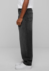 Black denim jeans with a relaxed fit, featuring a five-pocket design, subtle fading, and a straight leg shape. Paired with white sneakers.