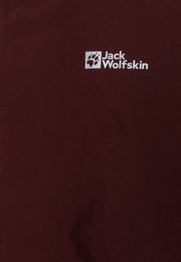 Giacca bordeaux con una texture liscia, dotata di un logo bianco "Jack Wolfskin" e dettagli di cucitura. Design semplice senza ulteriori accenti.
