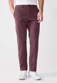 Mørkerøde chinos laget av bomull, med rett ben-design, frontlommer og knappelukking, sammen med hvite sneakers.