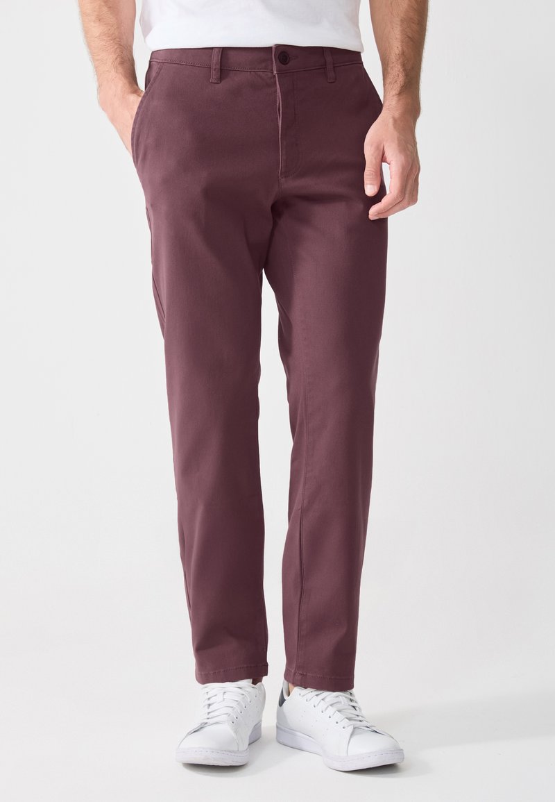 Mørkerøde chinos laget av bomull, med rett ben-design, frontlommer og knappelukking, sammen med hvite sneakers.