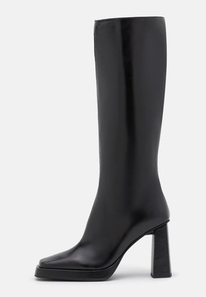 Botte noire jusqu'au genou avec une finition en cuir lisse et élégante, bout carré et talon bloc épais. Design minimaliste sans aucune pièce métallique visible.