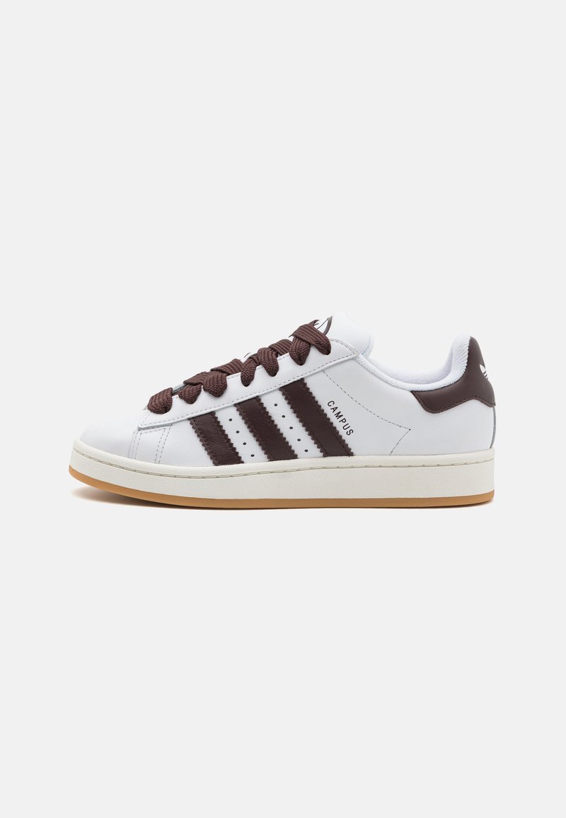 Baskets blanches en cuir avec des accents marron, présentant trois rayures noires, des lacets ronds et une semelle en caoutchouc. La vue de côté met en avant le détail du logo.